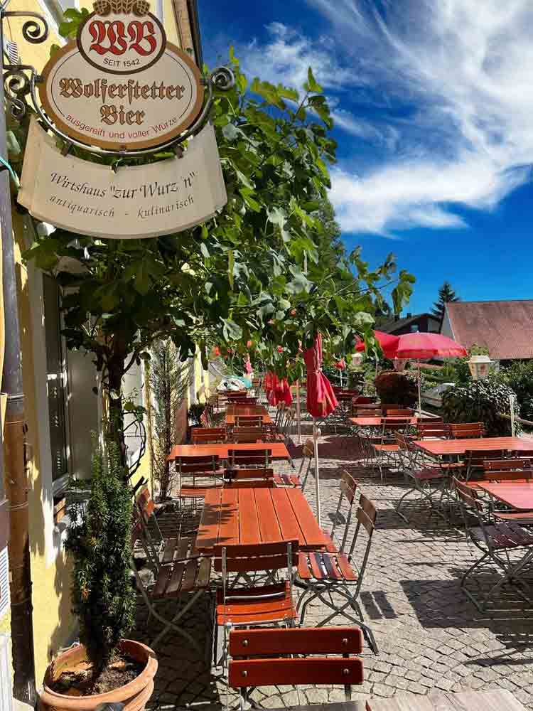 Biergarten der Wurz´n in Vilshofen mit Holztischen, roten Sonnenschirmen und historischem Wirtshausschild an der Fassade.